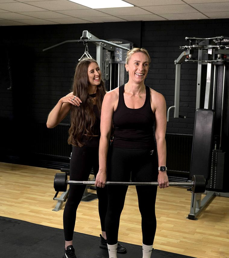 Elin Wyn standing with a client who is holding a barbell across her shoulders